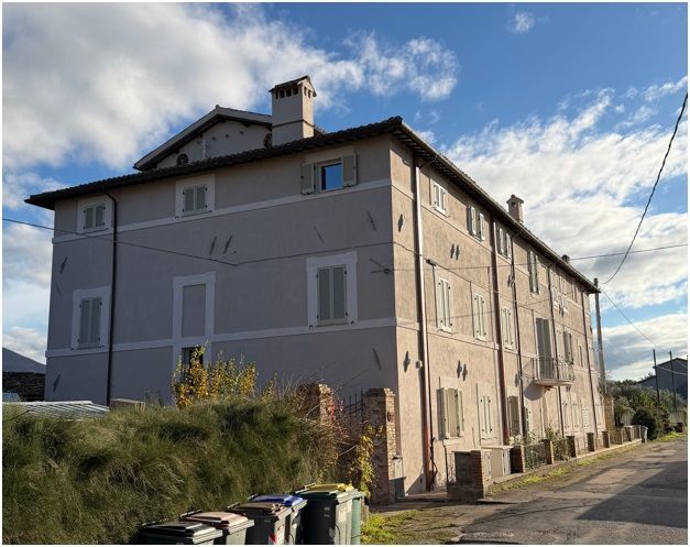 Edificio a più piani con facciata grigio chiaro, numerose finestre e cielo azzurro come sfondo.