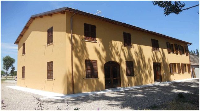 Edificio color marrone chiaro a due piani con persiane e porte marroni, in una giornata di sole.