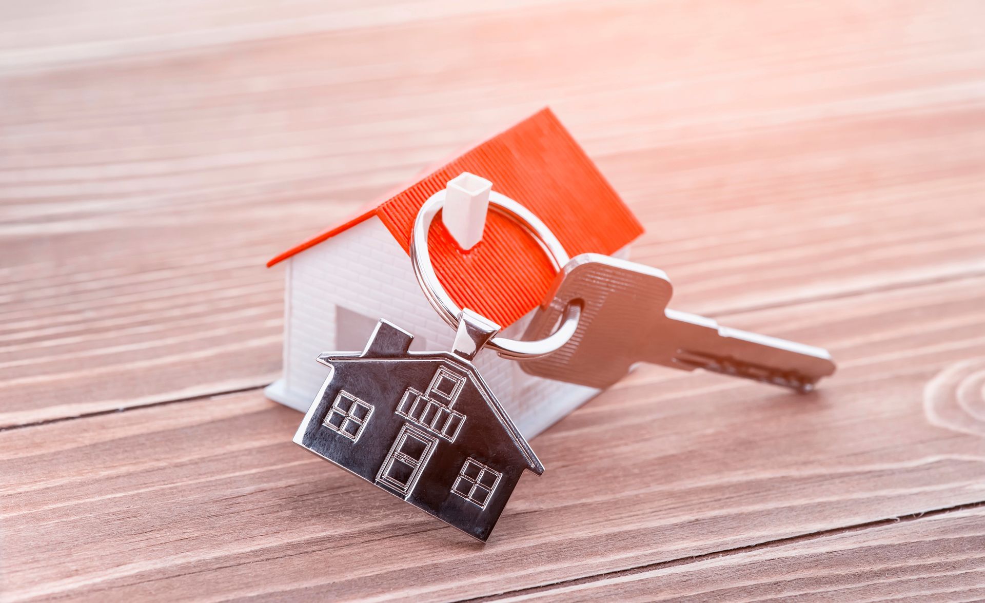 Casetta giocattolo con tetto rosso, portachiavi con ciondolo a forma di casa e chiave su una superficie di legno.