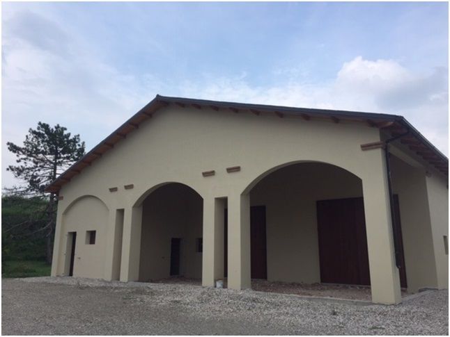 Edificio beige con aperture ad arco e porte marroni sotto un cielo nuvoloso.