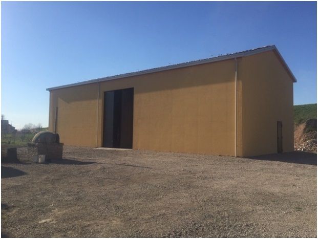 Edificio giallo con grande portone nero su ghiaia, cielo azzurro sullo sfondo.