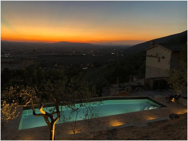 Una piscina al tramonto con vista su una valle dai colori arancione e blu scuro.
