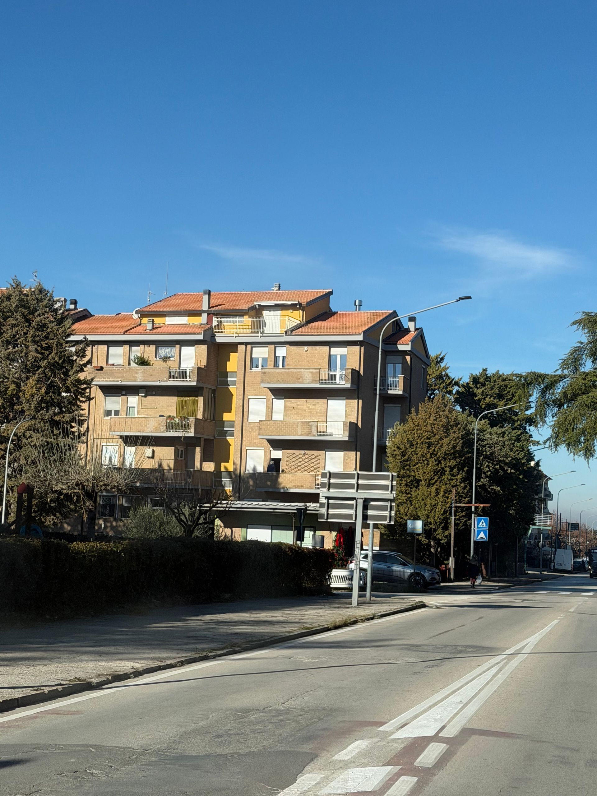 Condominio con balconi accanto a una strada, con un cielo azzurro brillante sopra.
