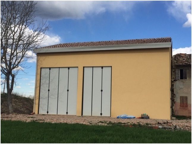 Edificio giallo con due portoni da garage contro il cielo azzurro, albero sulla sinistra.