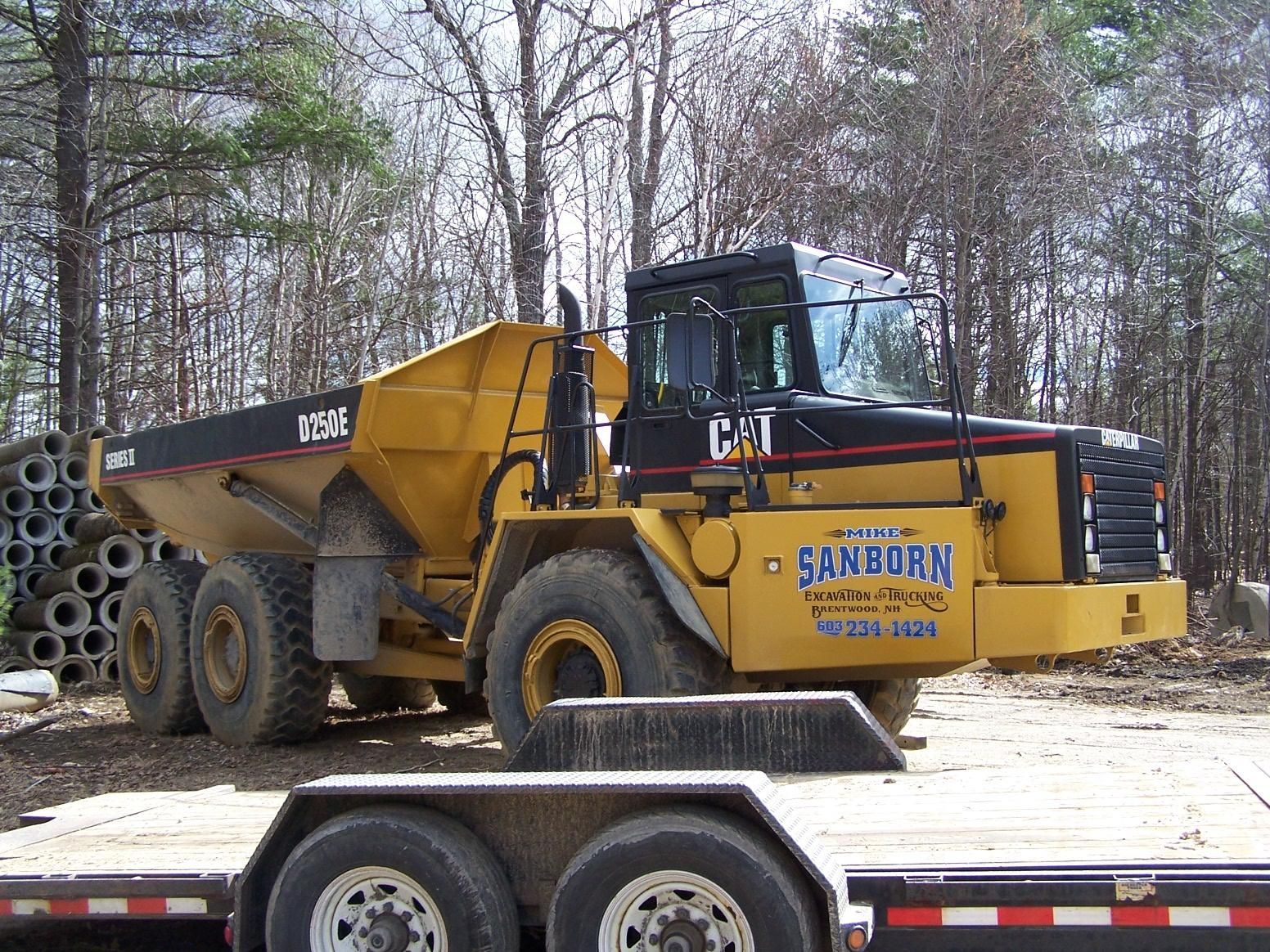 A cat dump truck is parked next to a trailer