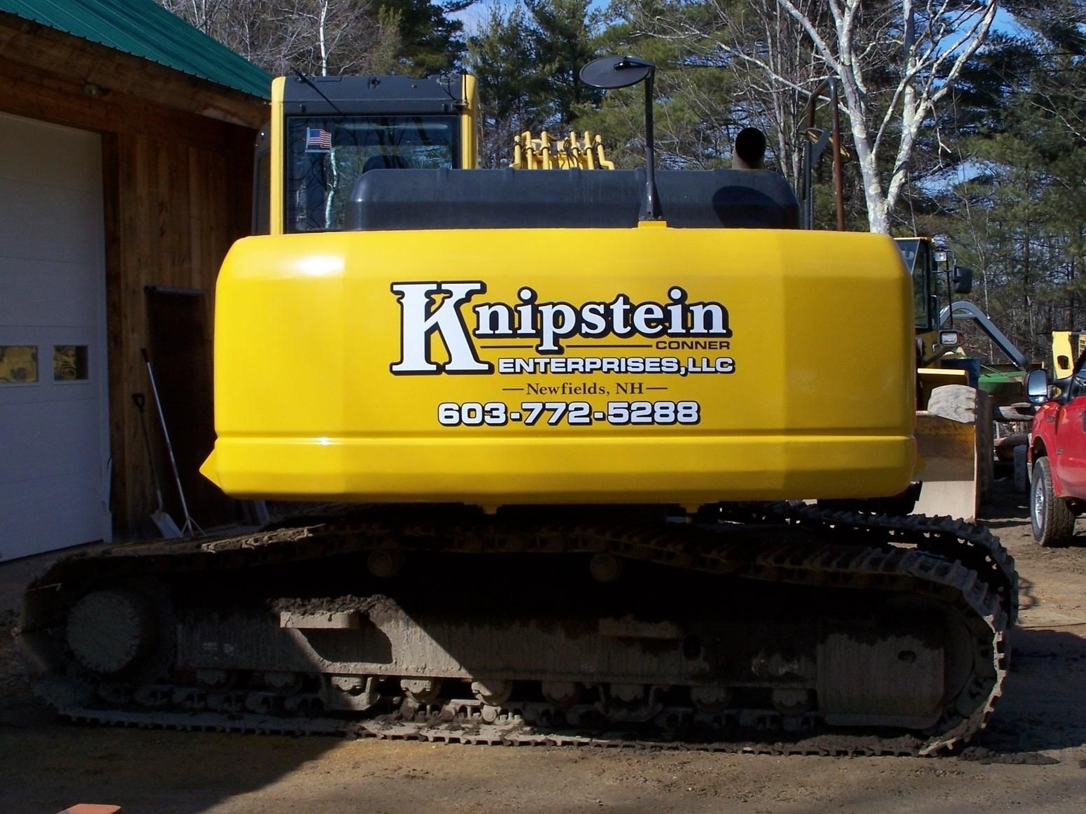 A yellow knipstein excavator is parked in front of a garage