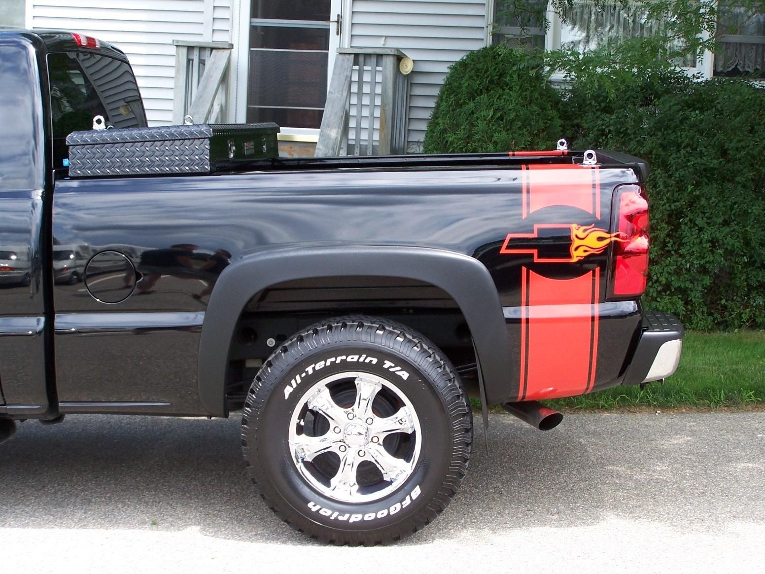 A black truck with a red stripe on the back is parked in front of a house