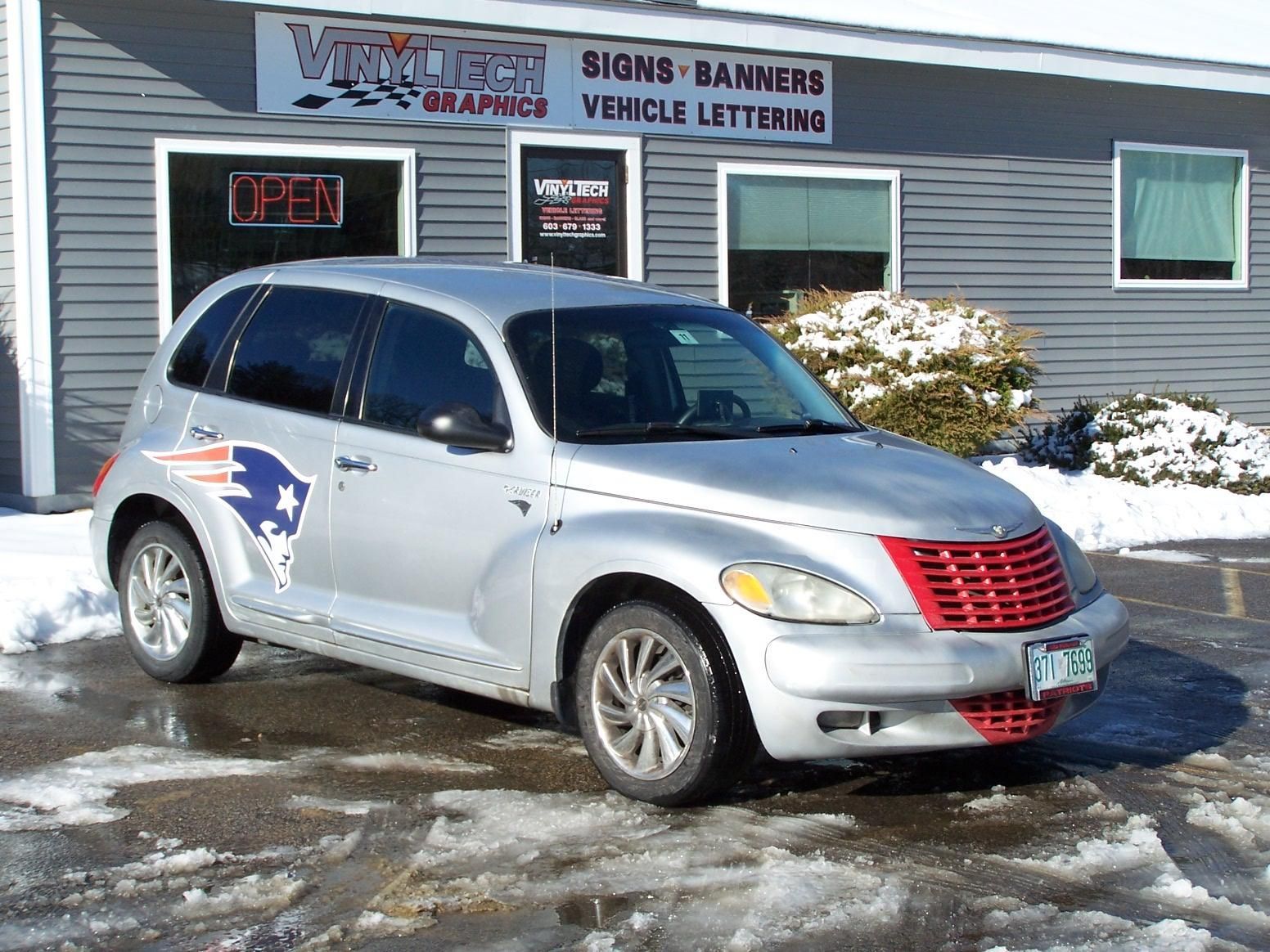 A silver car is parked in front of a store that sells signs banners and vehicle lettering