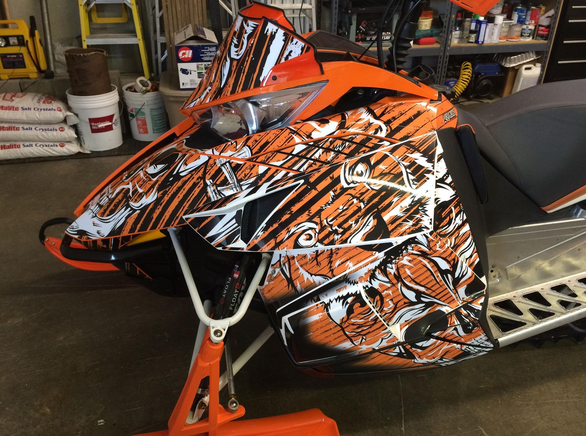 An orange and white snowmobile is parked in a garage