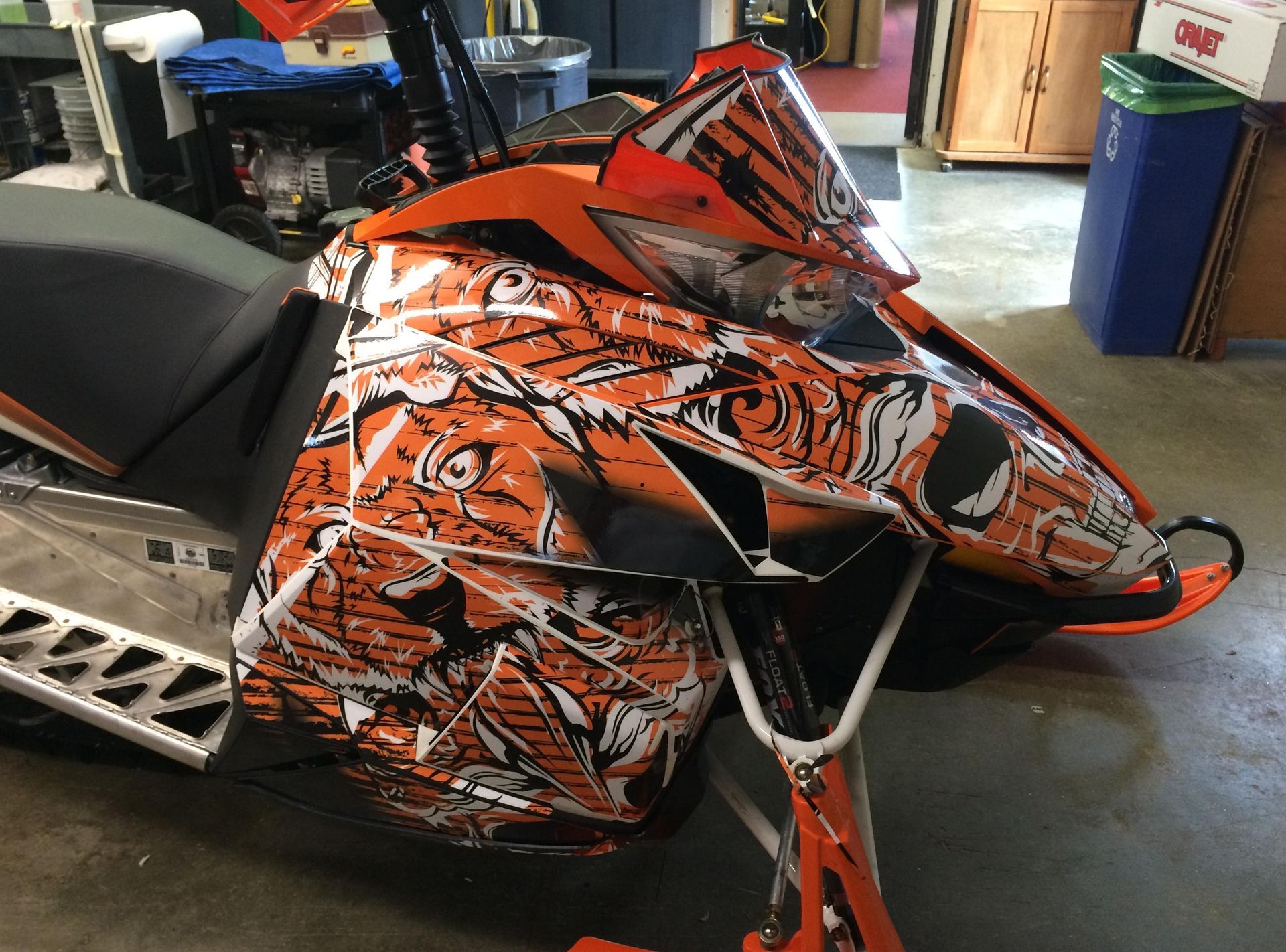 An orange and white snowmobile is parked in a garage