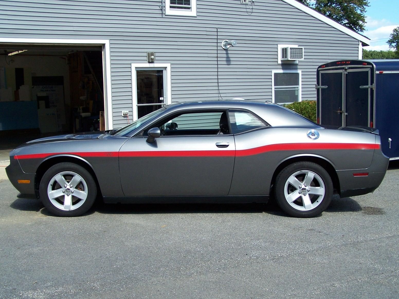 A gray and red dodge challenger is parked in front of a garage