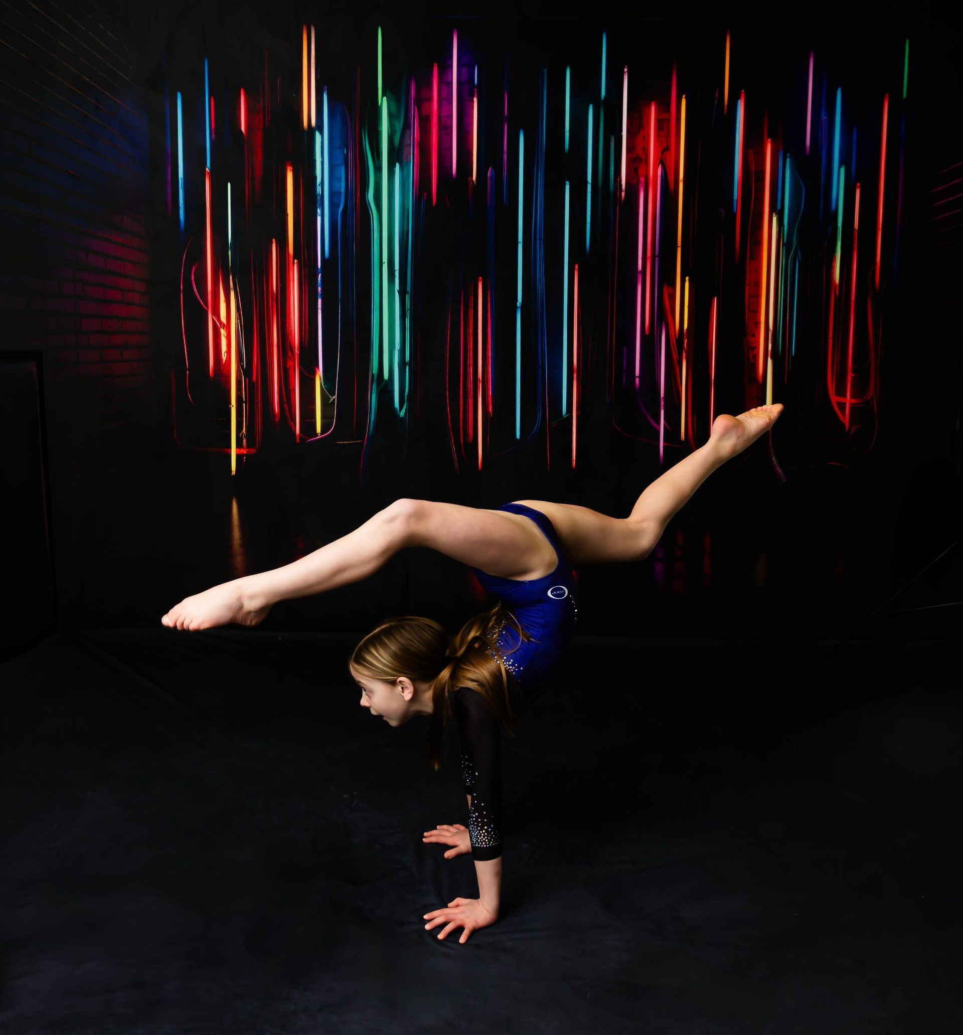 Gymnast in blue leotard performs a handstand split, colorful light backdrop.