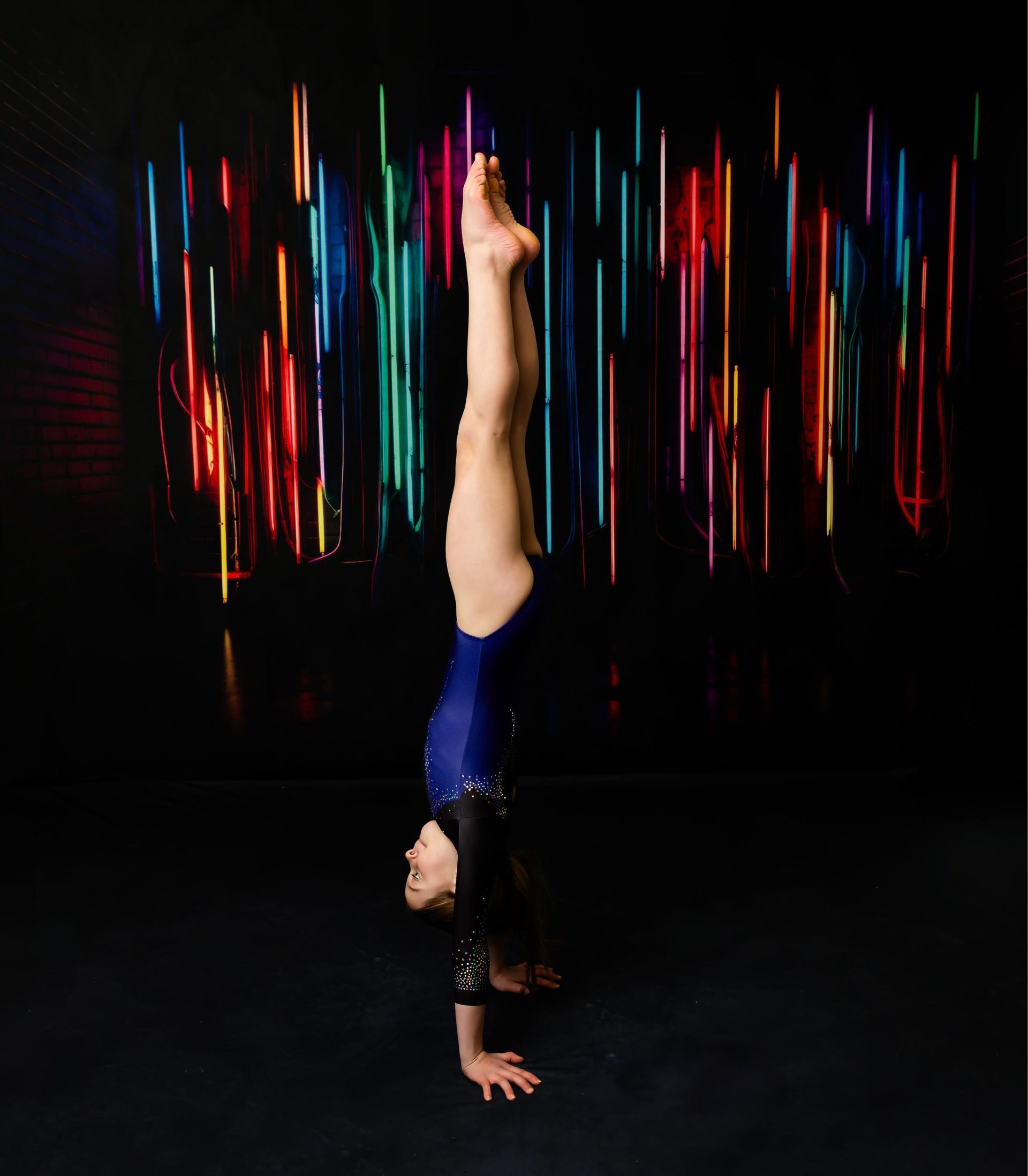 Gymnast in a handstand against a background of colorful vertical lights.