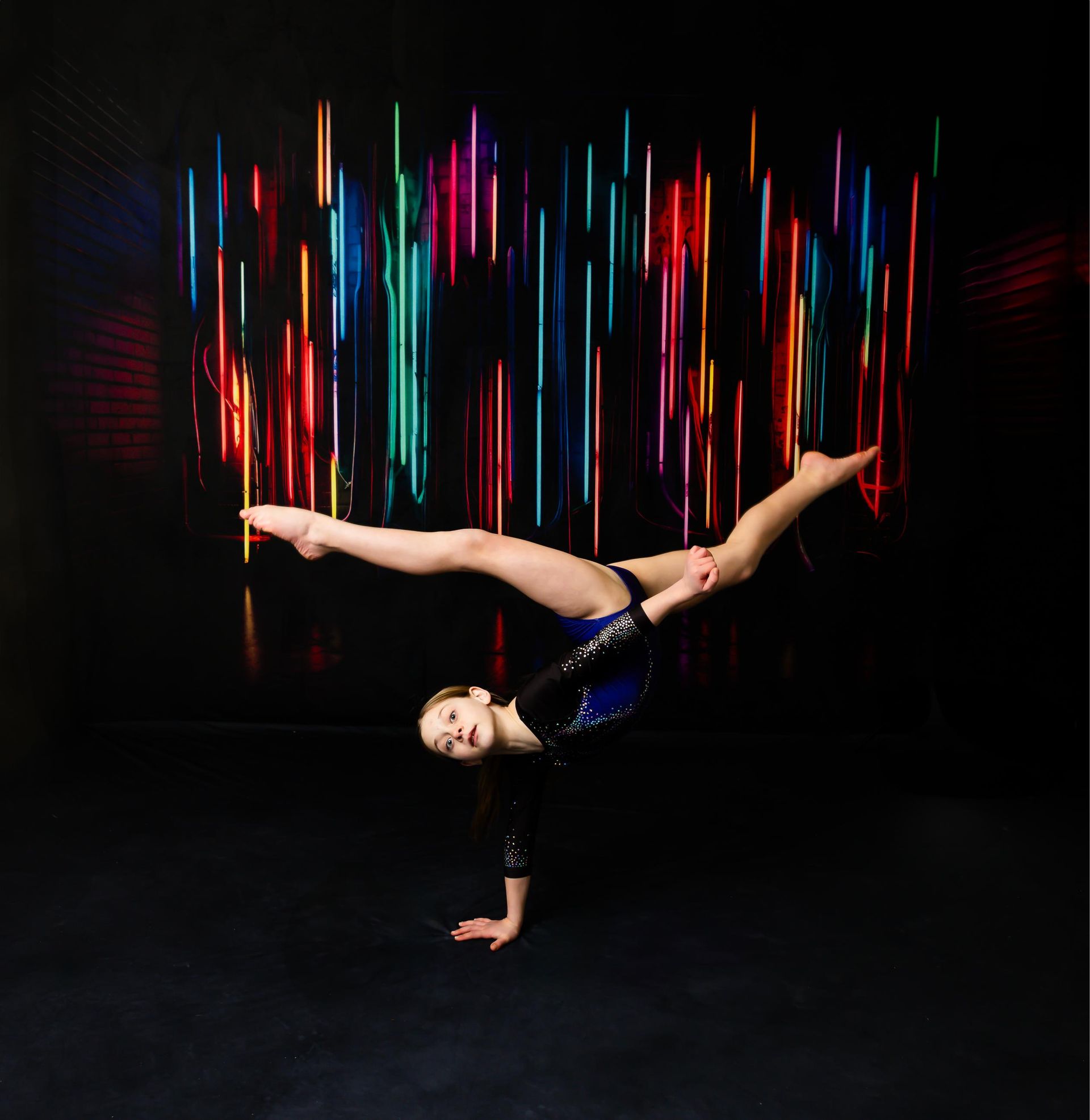 Gymnast doing a handstand split, colorful light streaks in the background.