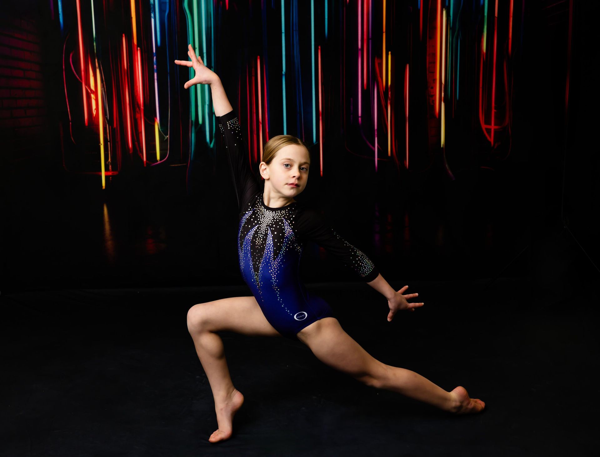 Gymnast in blue leotard, balancing, arm raised, with colorful light backdrop.