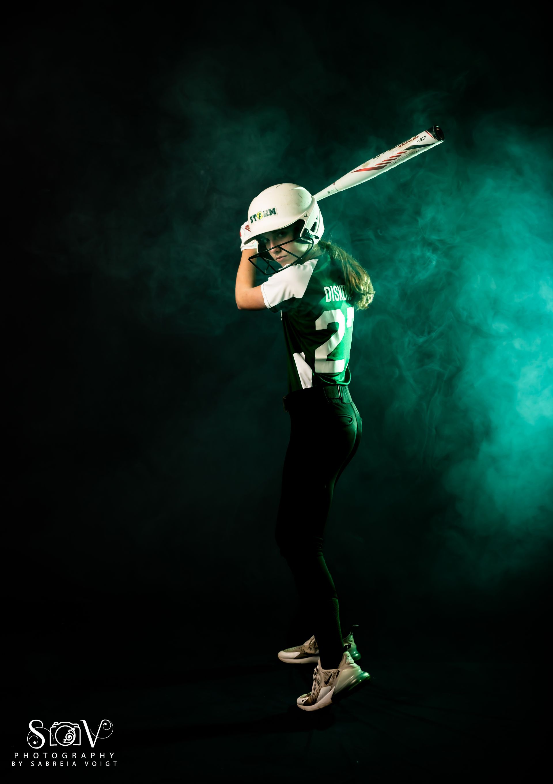 Softball player in uniform holding bat, ready to swing against a teal-lit, smoky background.