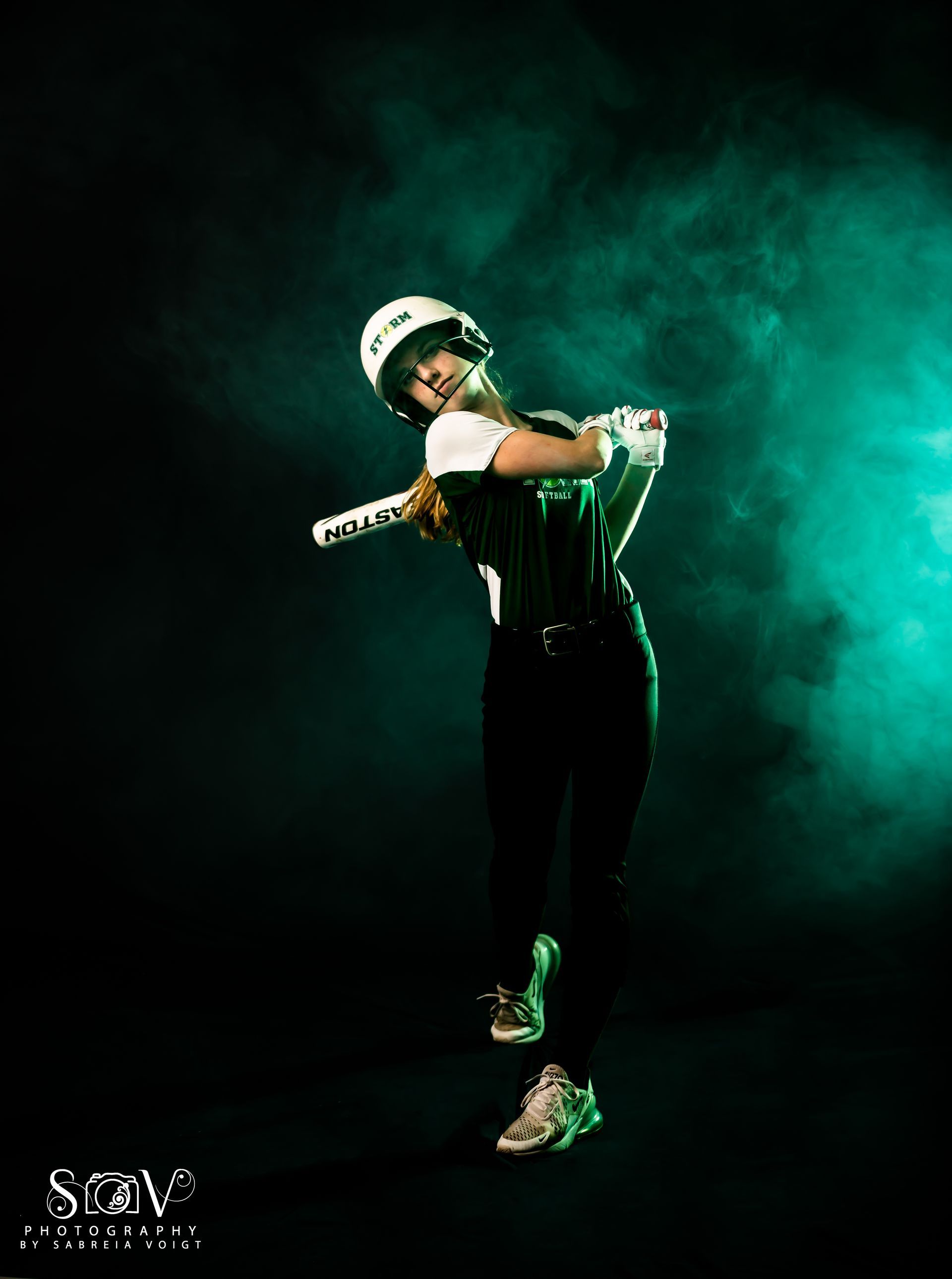 Softball player in uniform swinging bat, green-tinted background with smoke.