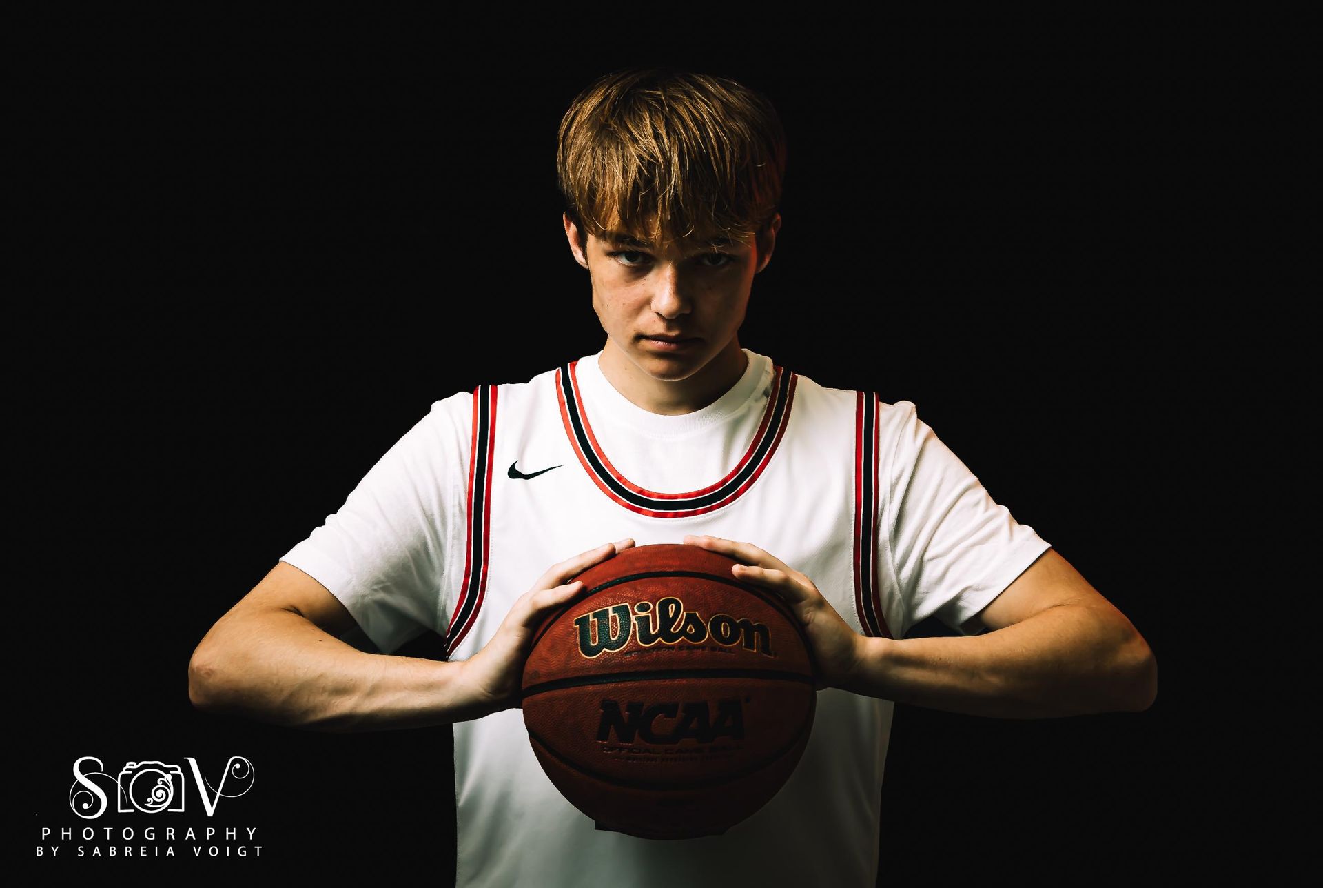 Basketball player holding a basketball, wearing a white jersey against a black backdrop.