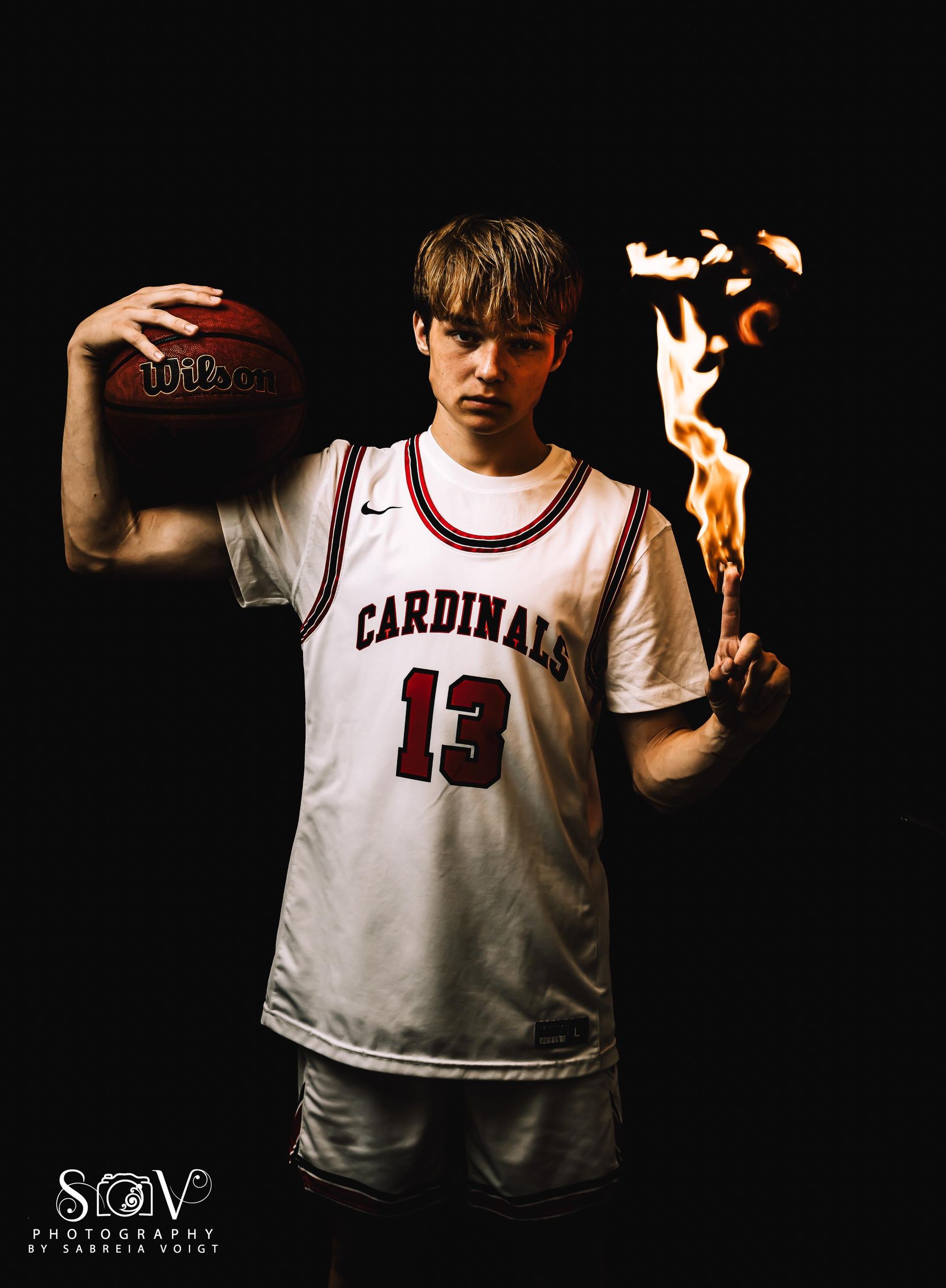 Basketball player in a jersey holding a ball with one hand and a lit torch with the other against a black background.