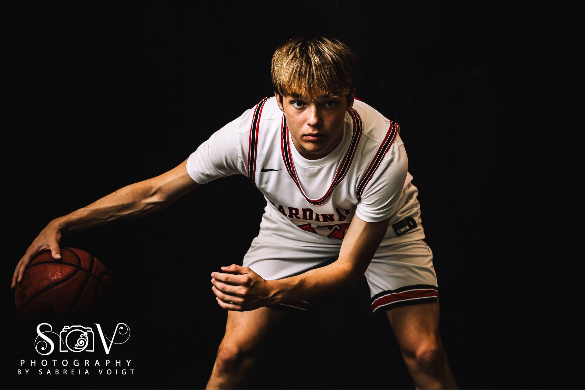 Basketball player dribbling, wearing white jersey with red trim, dark background.