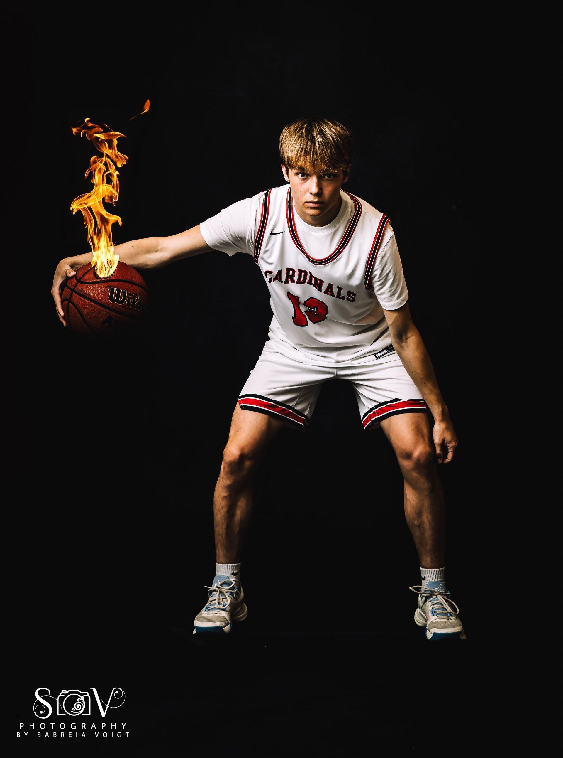 Basketball player dribbles a flaming ball against a black backdrop, wearing a white uniform with red trim.