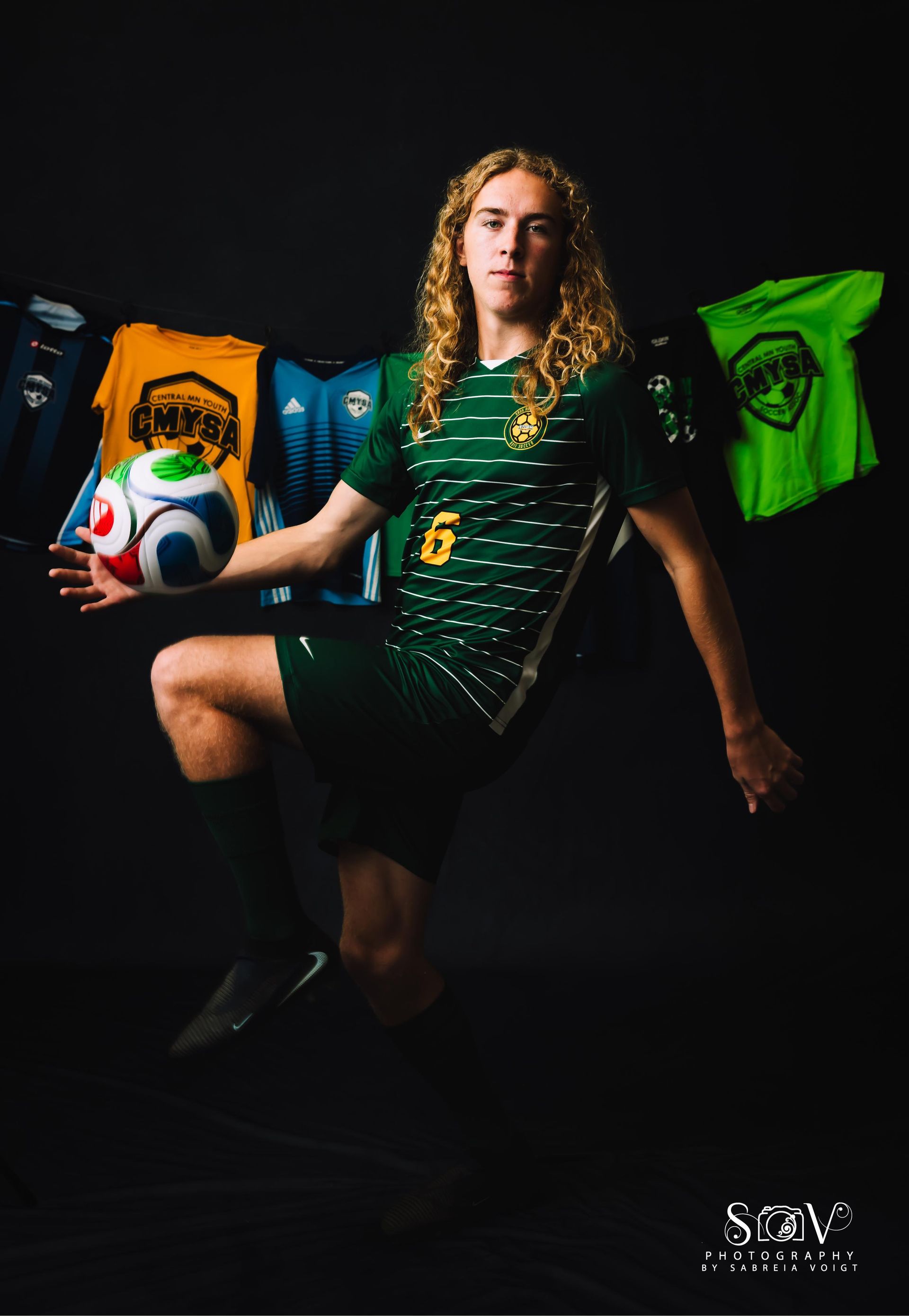 Soccer player in green jersey with ball, jumping, jerseys behind him.