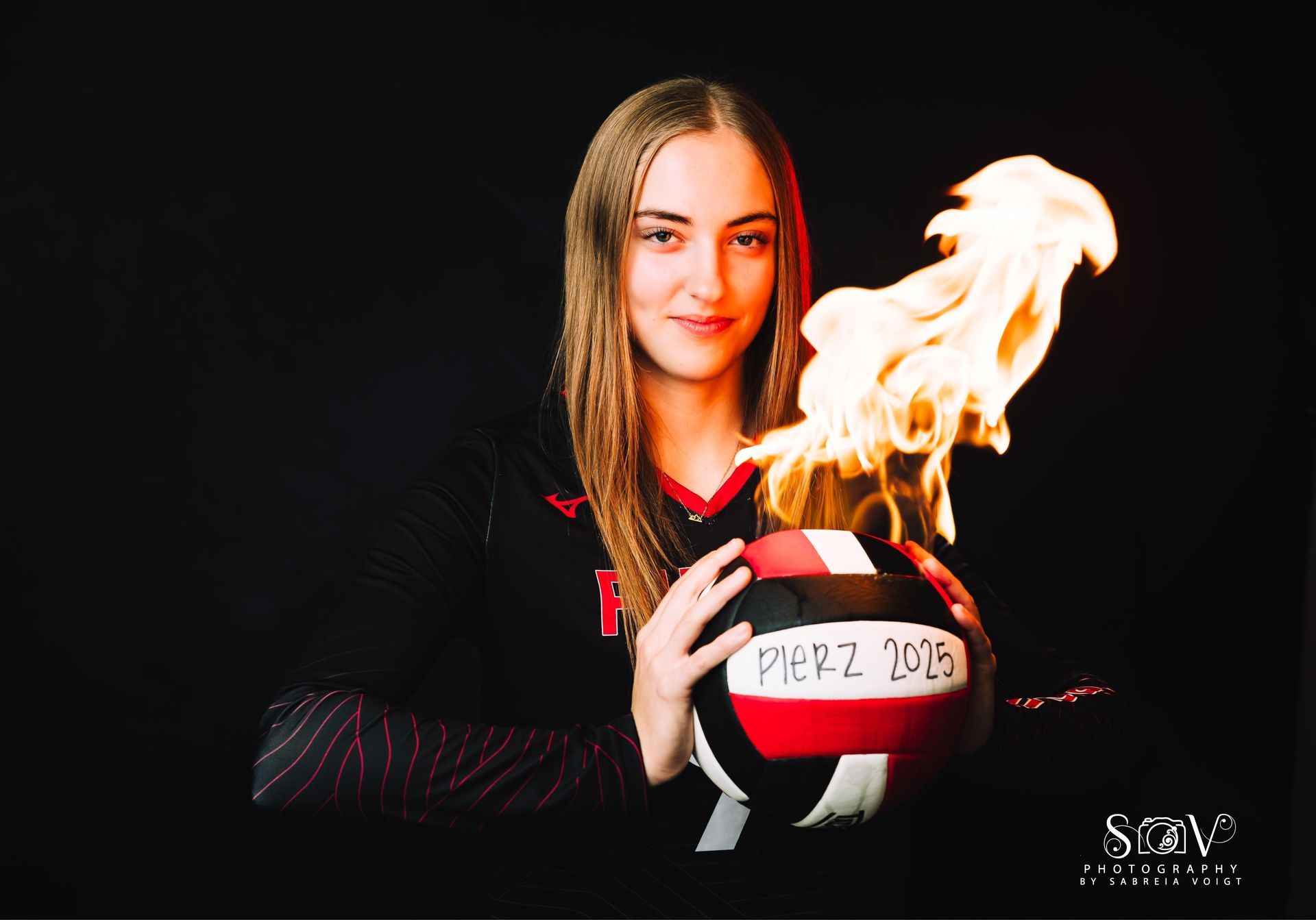 Volleyball player holding a flaming volleyball against a black background.