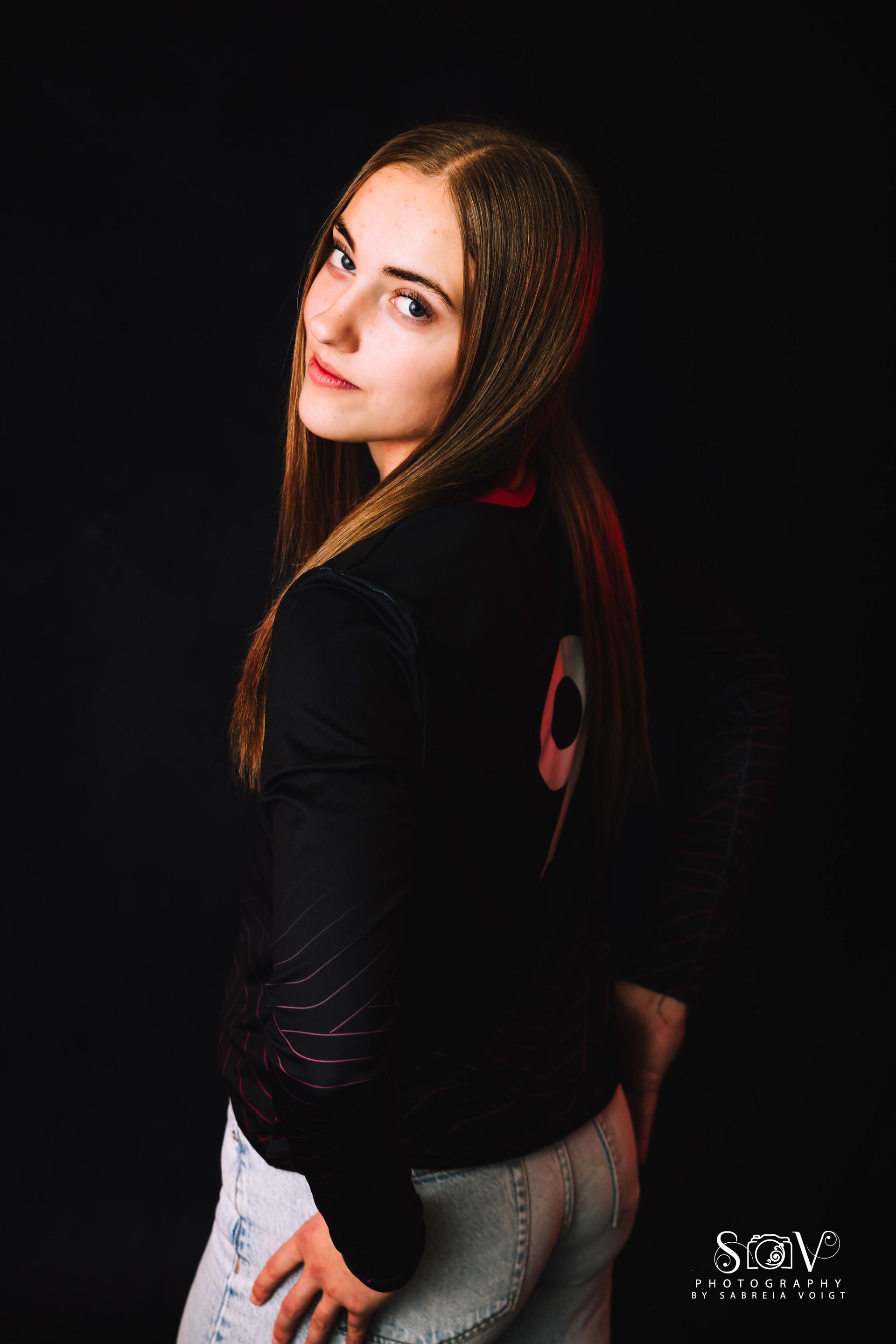 Woman with long hair and a black jacket, number 9 on back, looking over her shoulder.