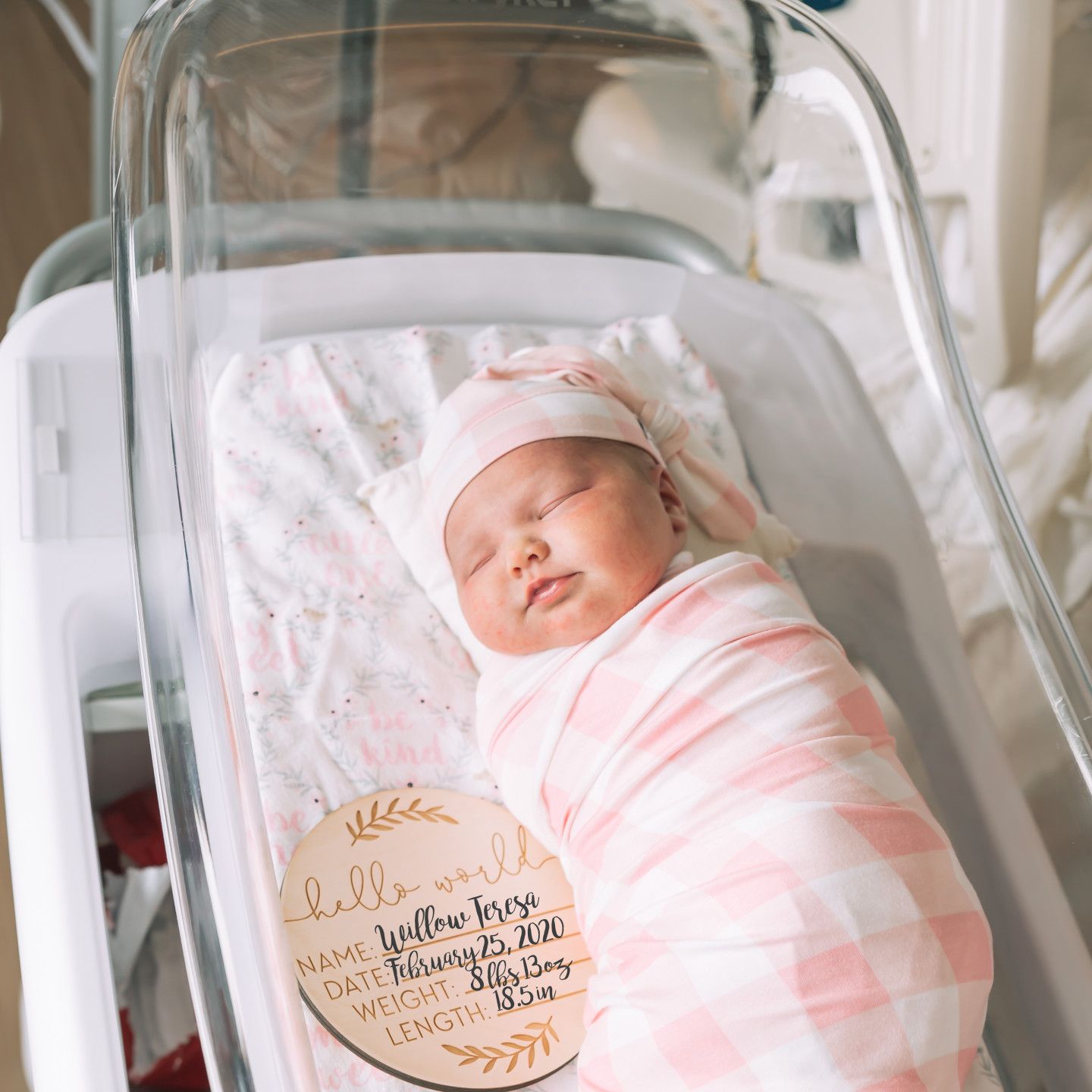 Newborn baby swaddled in pink, asleep in a hospital bassinet.