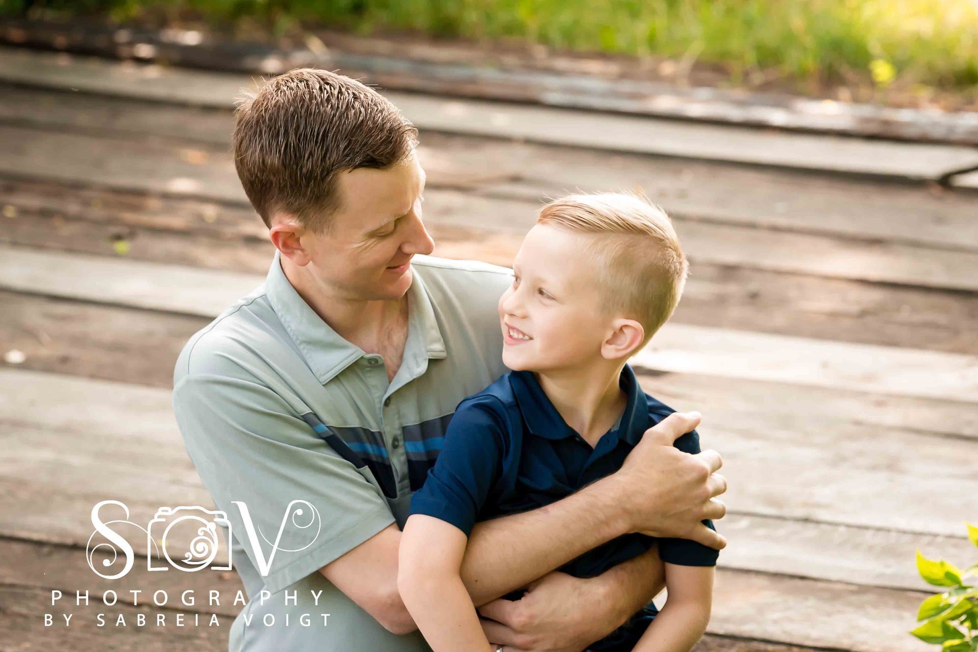 Father and son embrace outdoors, smiling at each other on wooden steps.