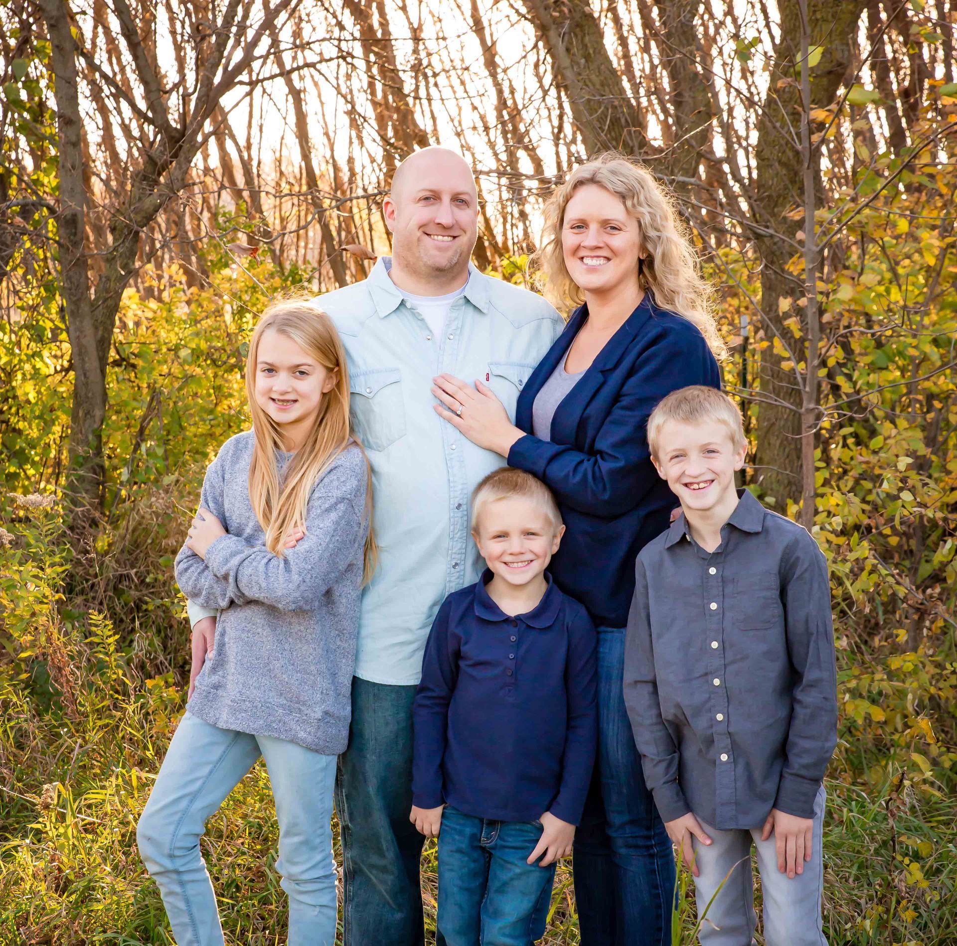 Family of five posing outdoors in front of fall foliage.