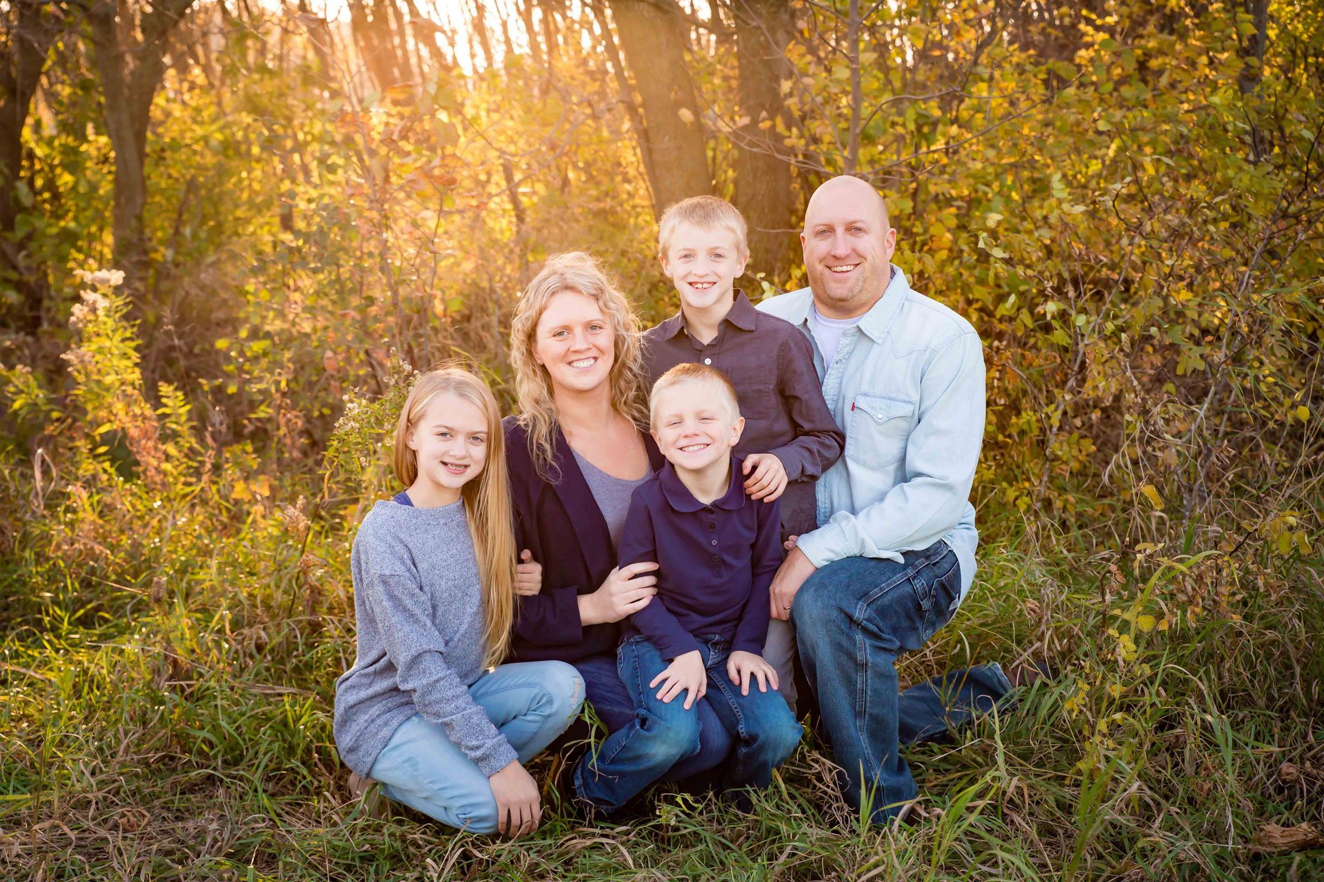 Family of five smiling outdoors in front of golden foliage.