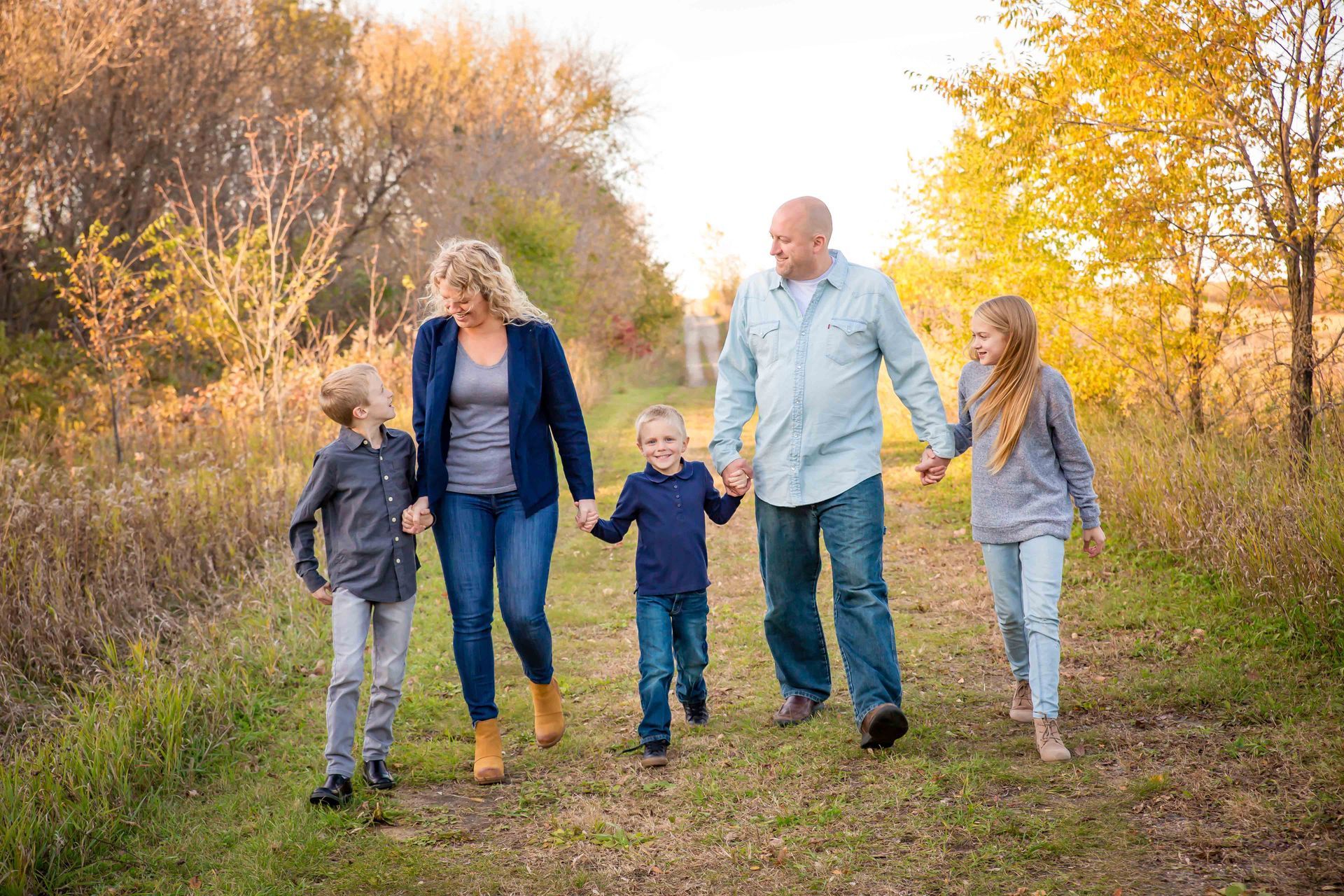 Family of five walks on a path outdoors, holding hands.