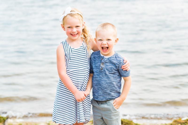 Girl in striped dress and boy laughing by the water.