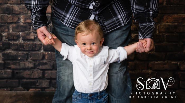 Child being held by an adult wearing a plaid shirt, standing in front of a brick wall.