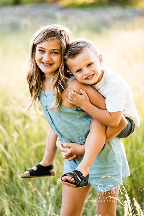 Girl giving piggyback ride to a boy in a field of tall grass; both smiling.