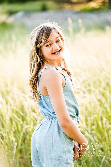Girl smiling in blue jumpsuit, standing in field of tall grass.
