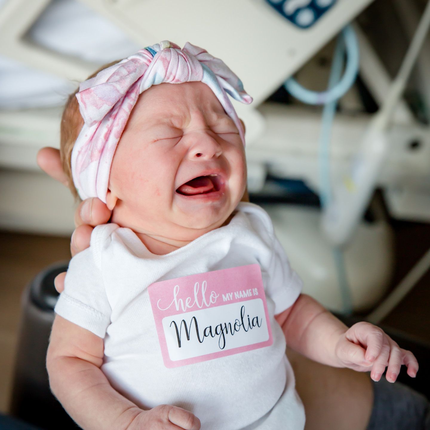 Newborn in hospital, crying, wearing a pink bow and 