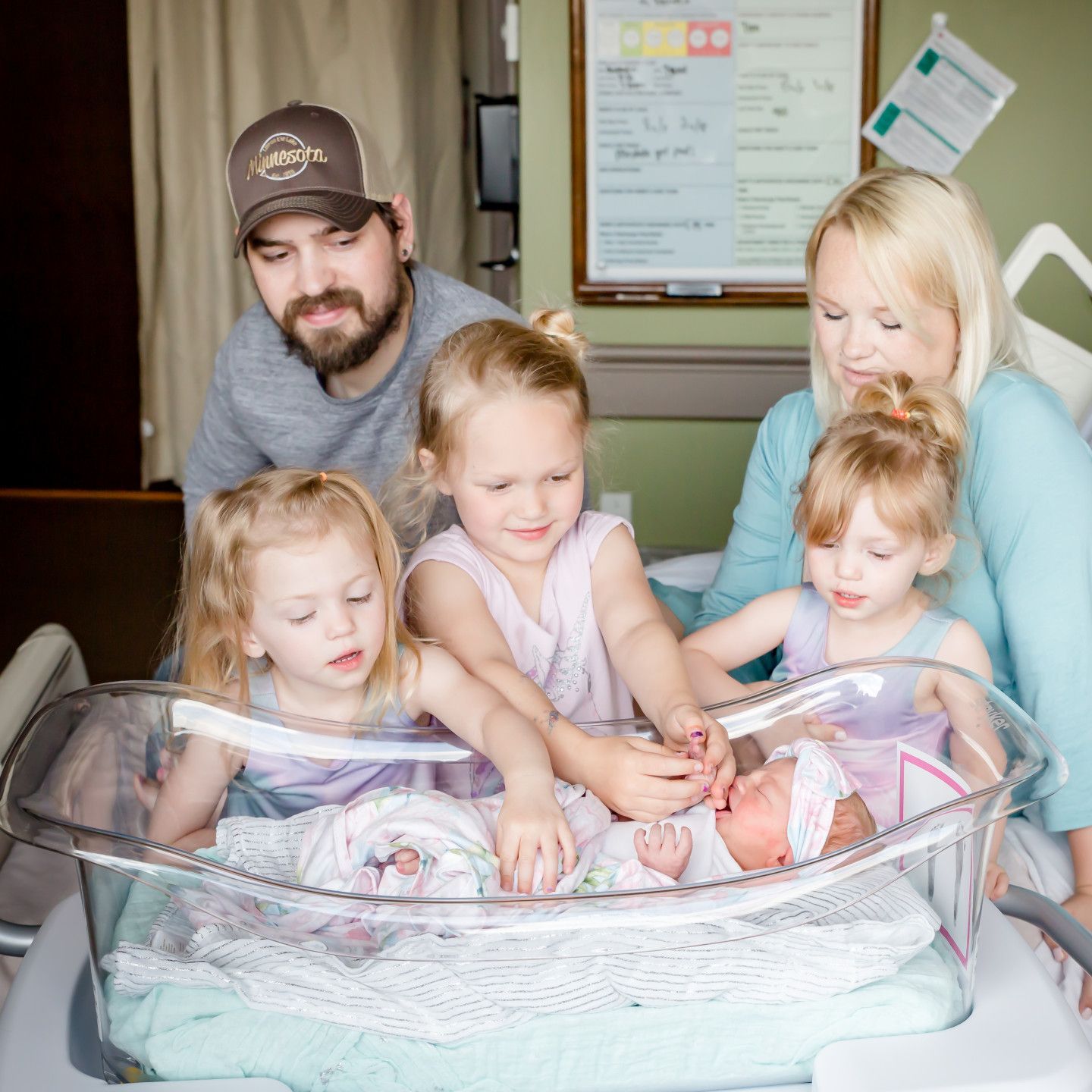 Family of six in hospital room, admiring newborn baby in bassinet.