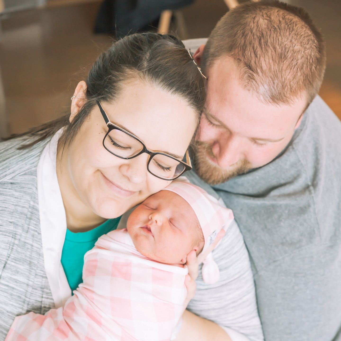 Parents holding newborn baby wrapped in a pink blanket. They are smiling.