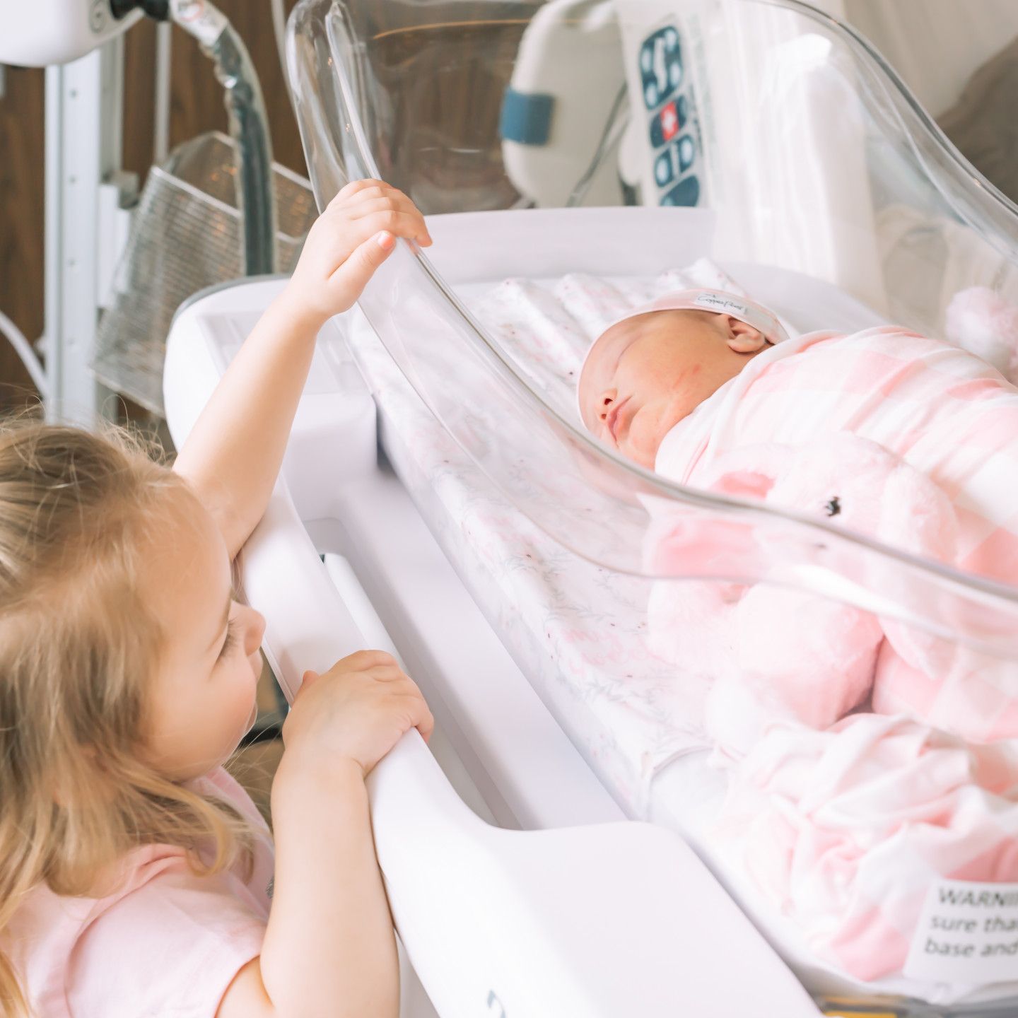 Girl looking at a newborn baby in a hospital bassinet.