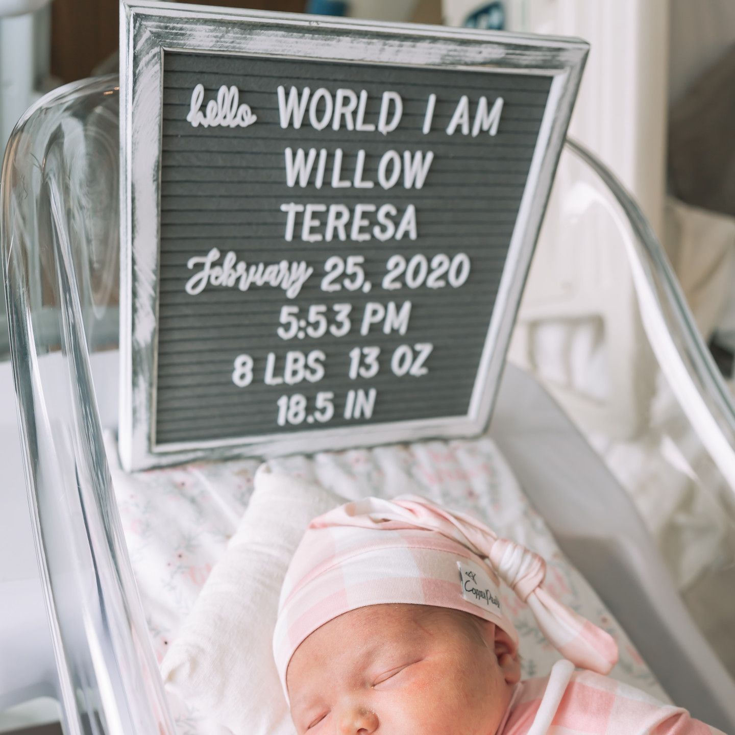 Newborn in a bassinet next to a sign that says 