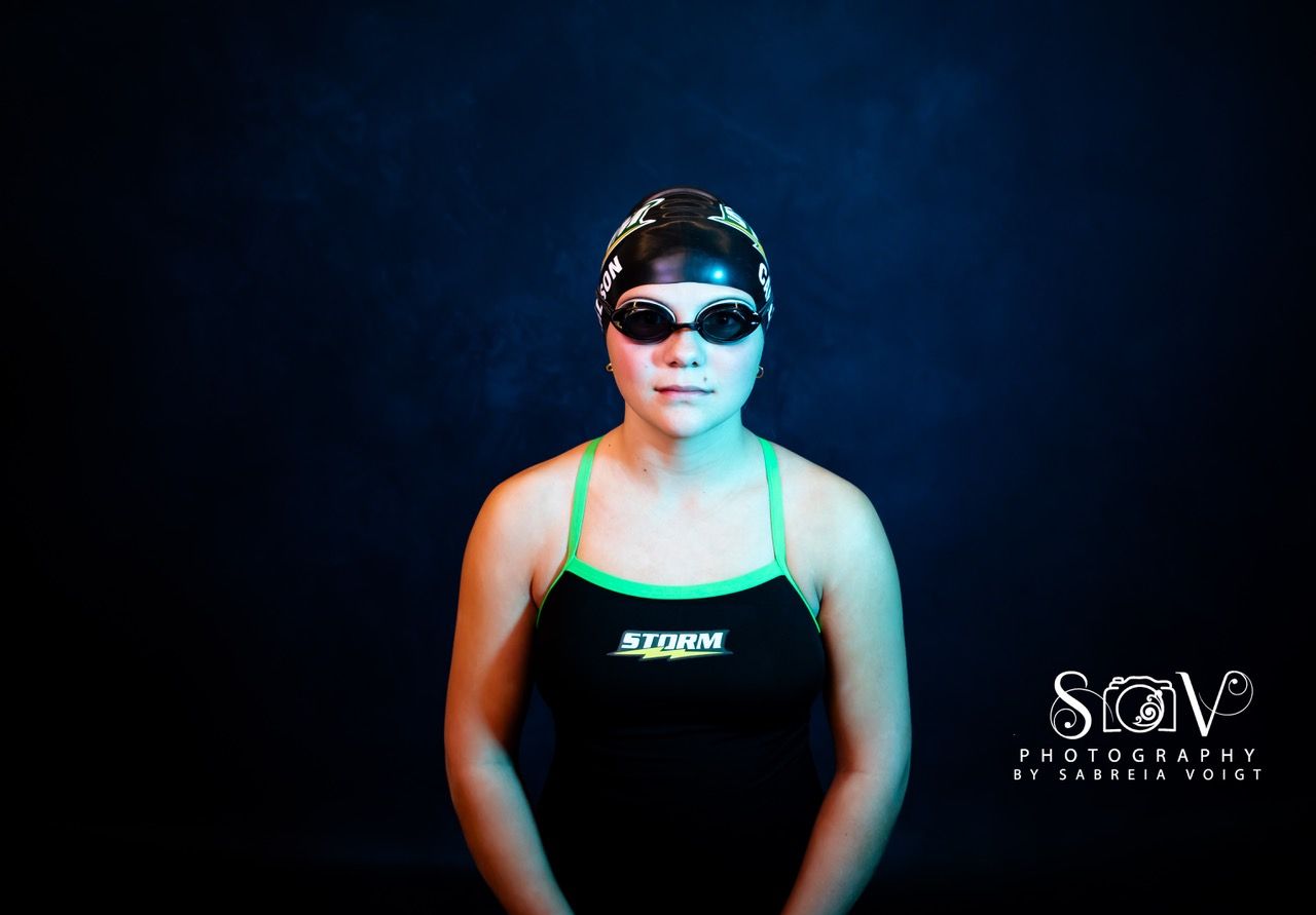 Swimmer wearing goggles and cap against a dark background, lit with blue and green light.