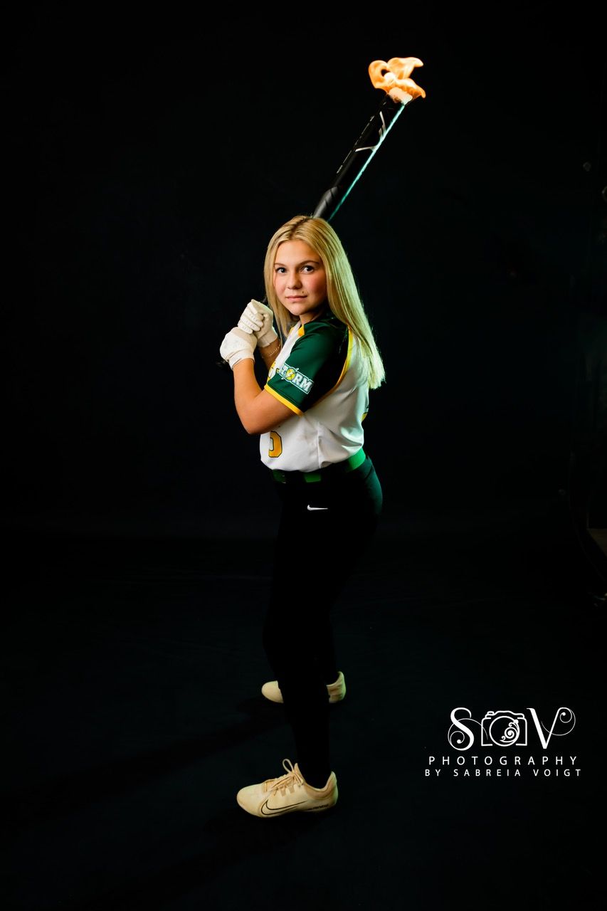 Softball player in uniform holding bat, studio shot with green and gold accents.