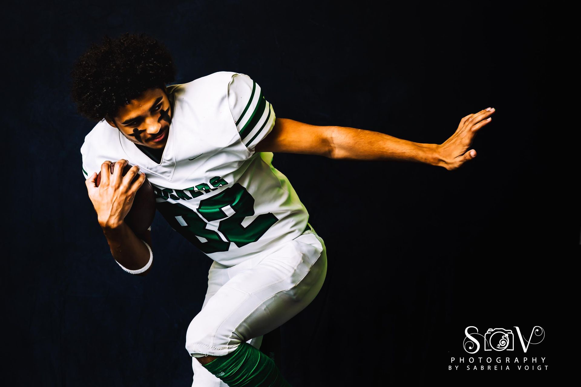 Football player in white and green uniform holding a ball.