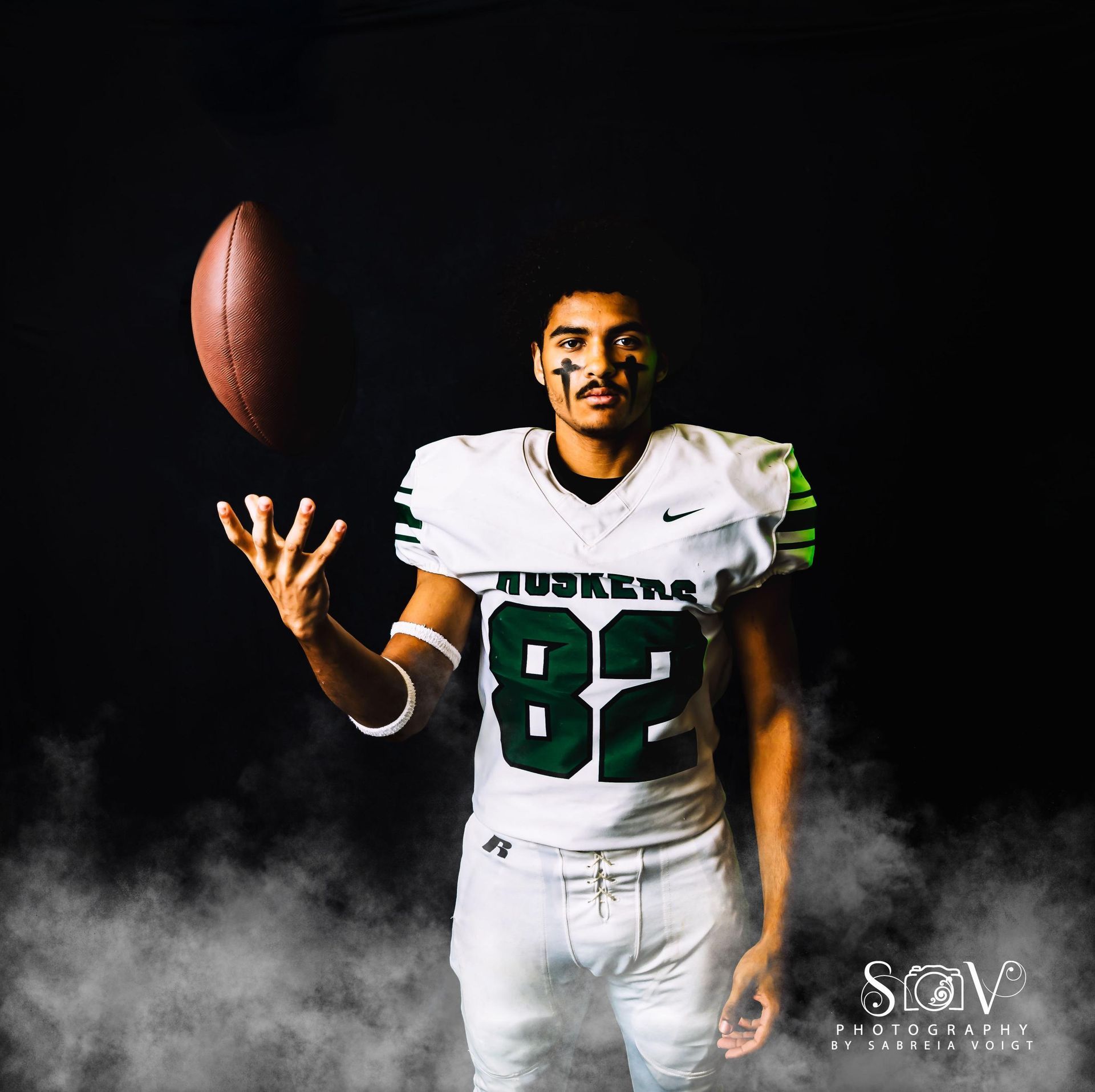 Football player in white jersey with green accents, catching ball, dark background with fog.