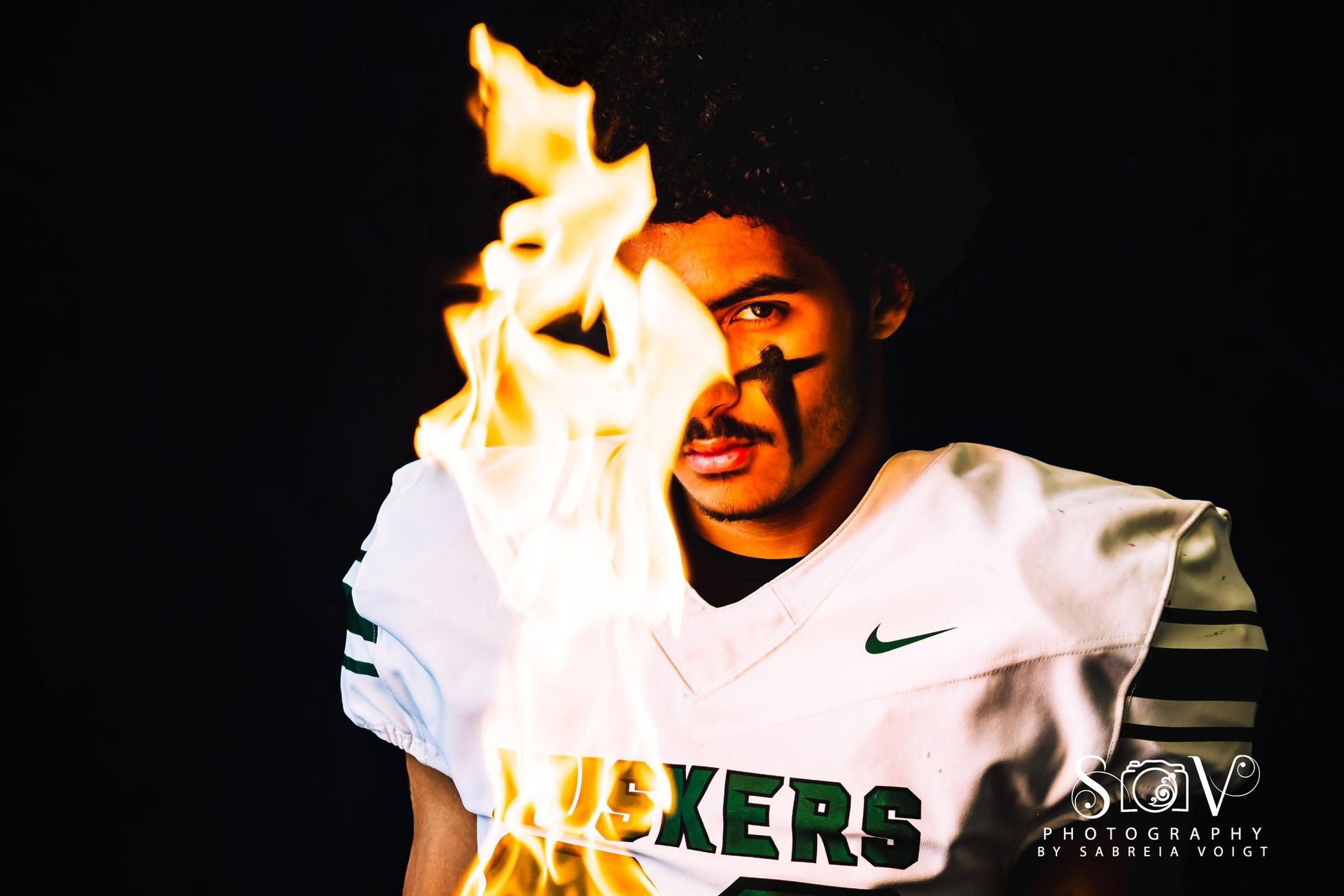 Football player with flames in front of face. White jersey with green trim and 