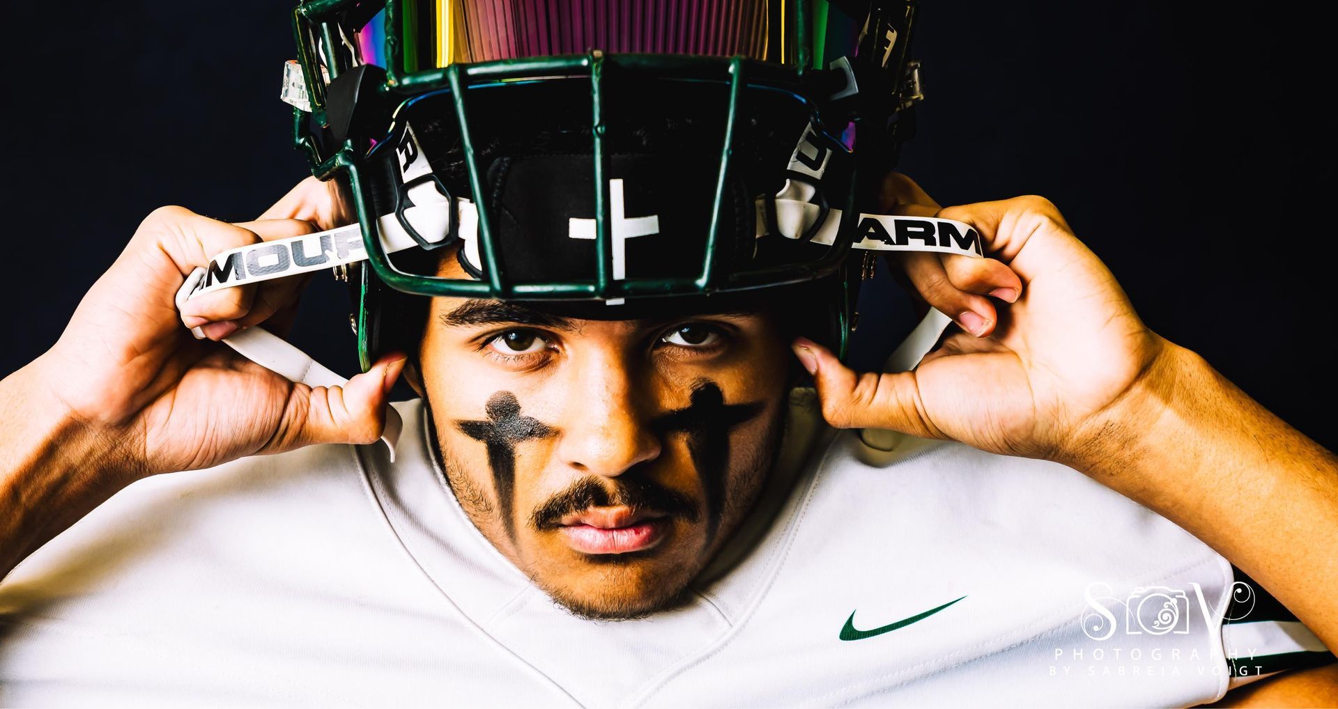 Football player adjusting helmet, face paint, green and black colors.