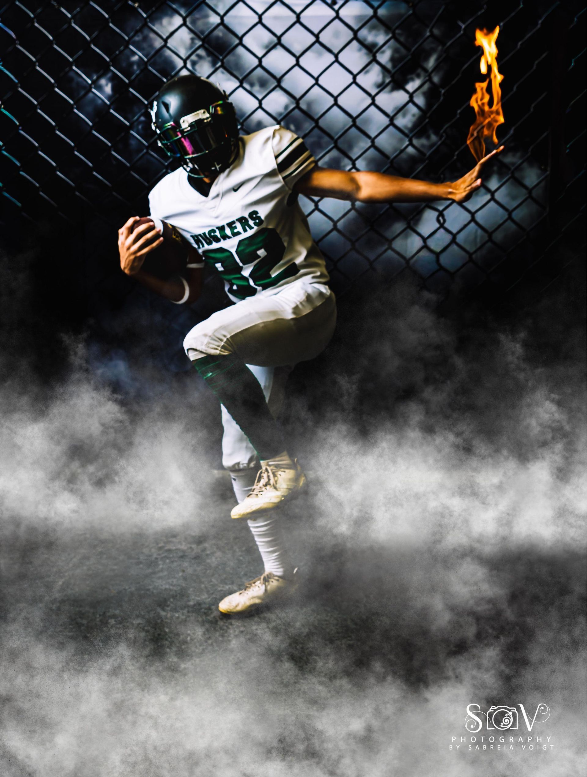 Football player in a white and green uniform holding a ball, running with flame effect and smoky background.