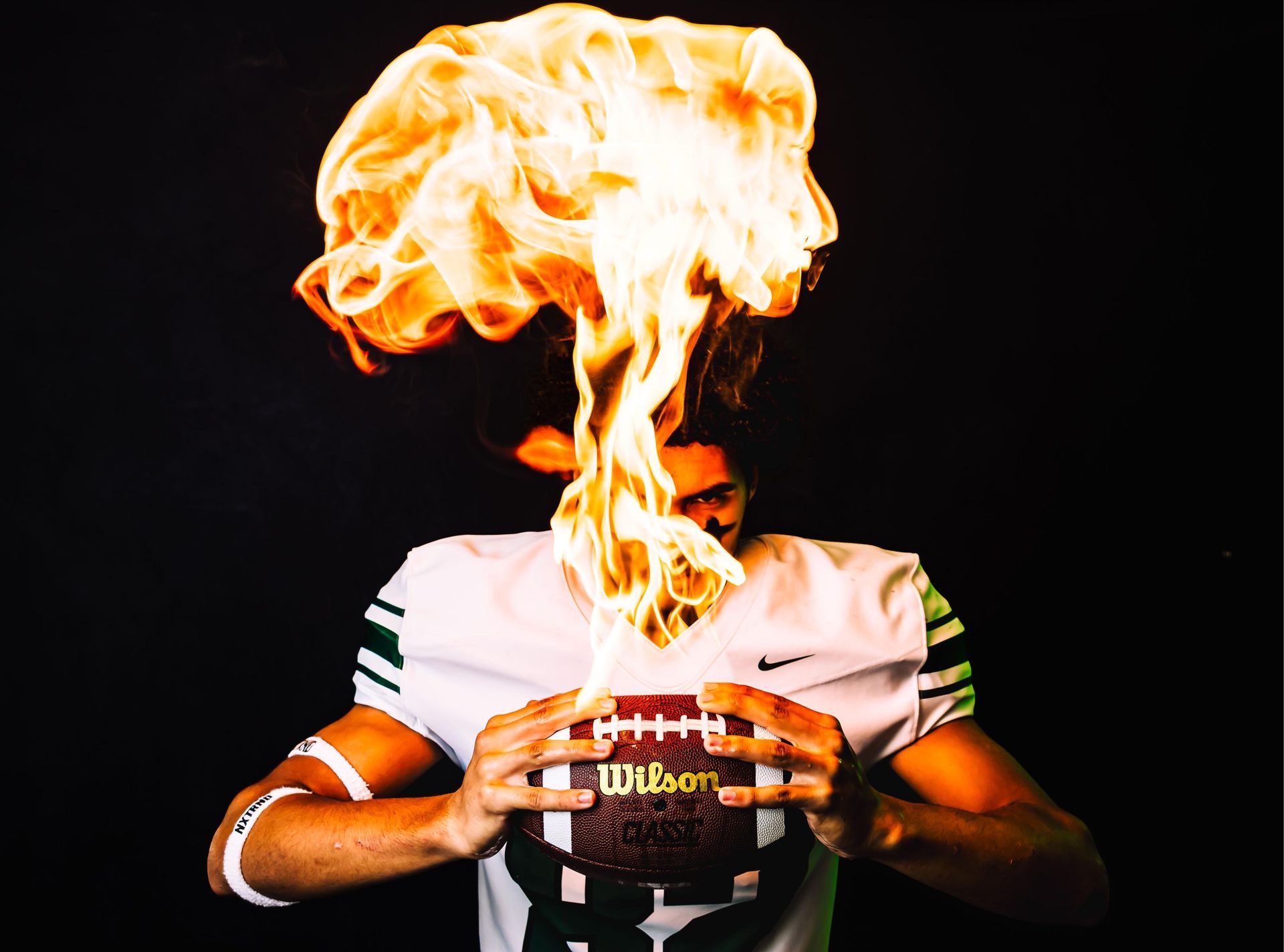 Football player holding football with flames erupting over his head.
